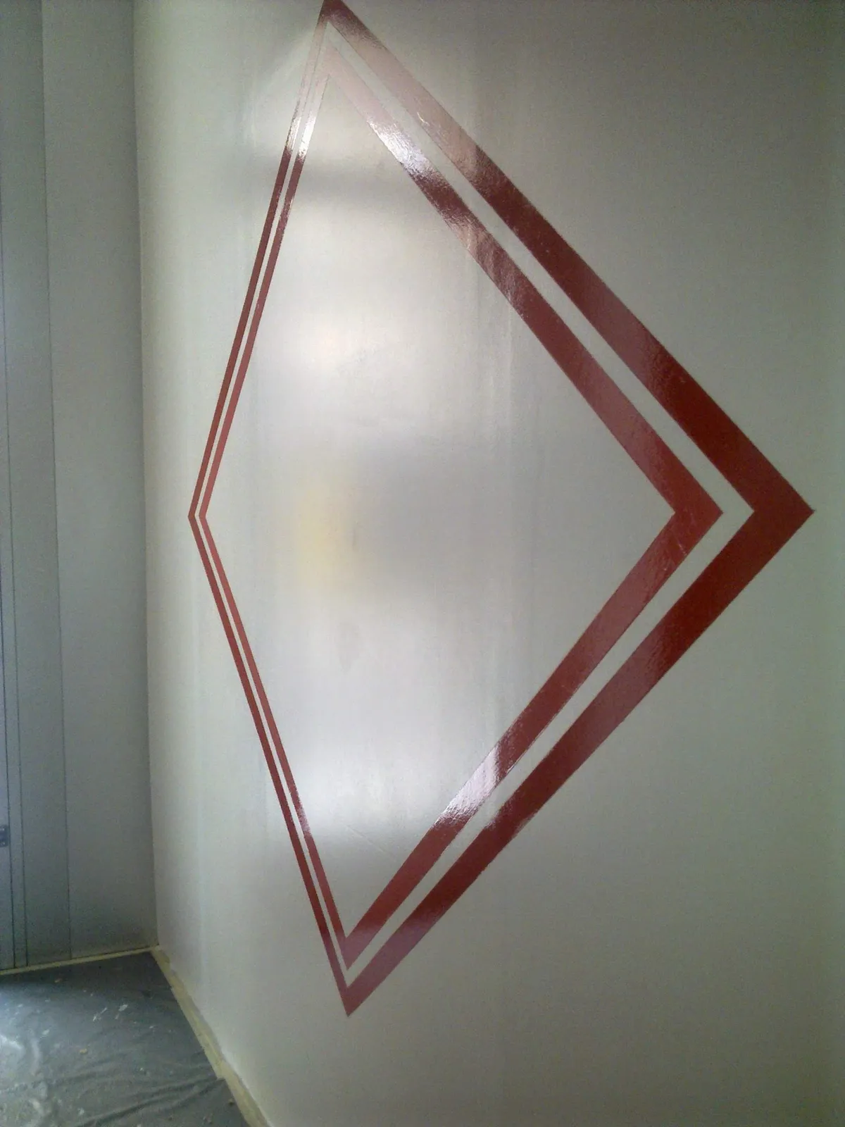 Motif géométrique en losange rouge peint sur un mur blanc, un effet décoratif graphique typique de la peinture décorative.