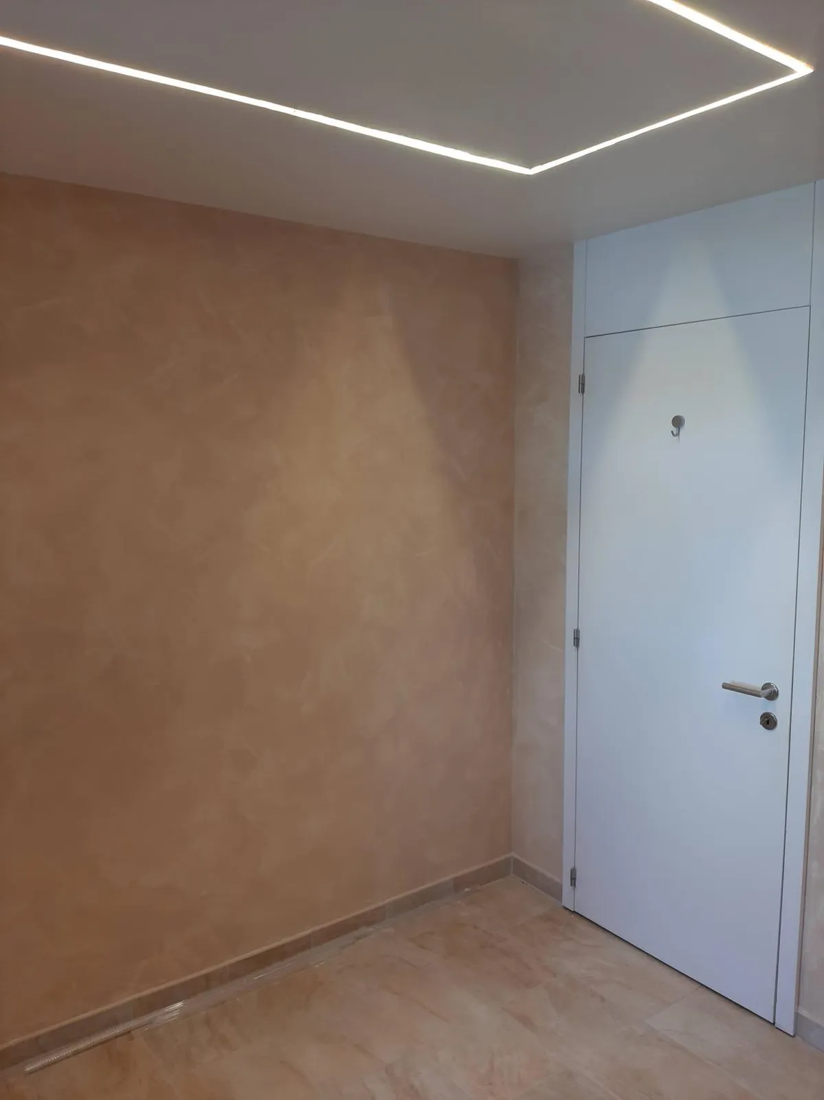 Mur d'entrée en enduit décoratif terracotta aux nuances douces, porte blanche et plafond à gorge lumineuse, réalisation Peinture Casabene.