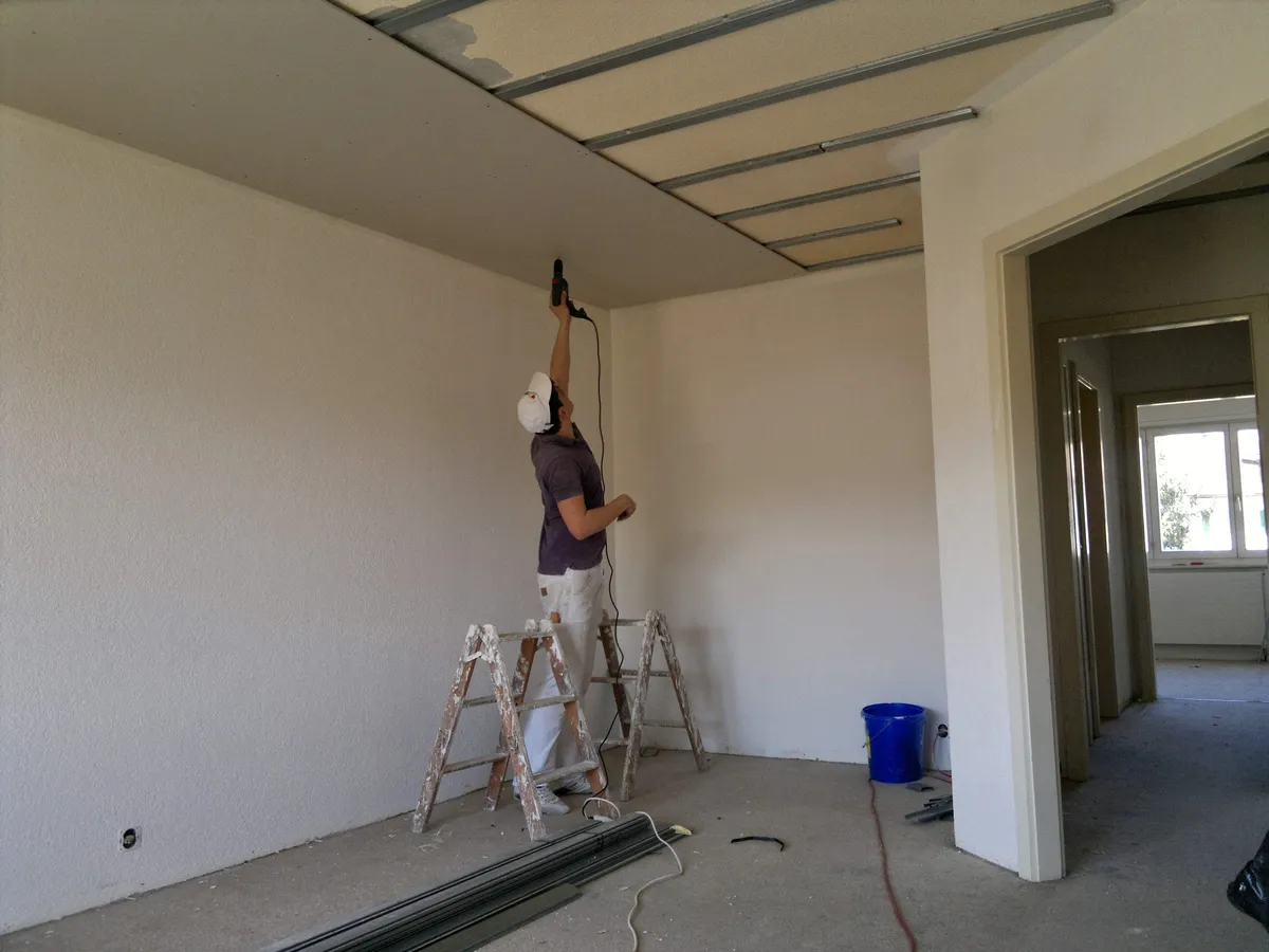 Deux plâtriers installant l'ossature métallique d'un faux plafond