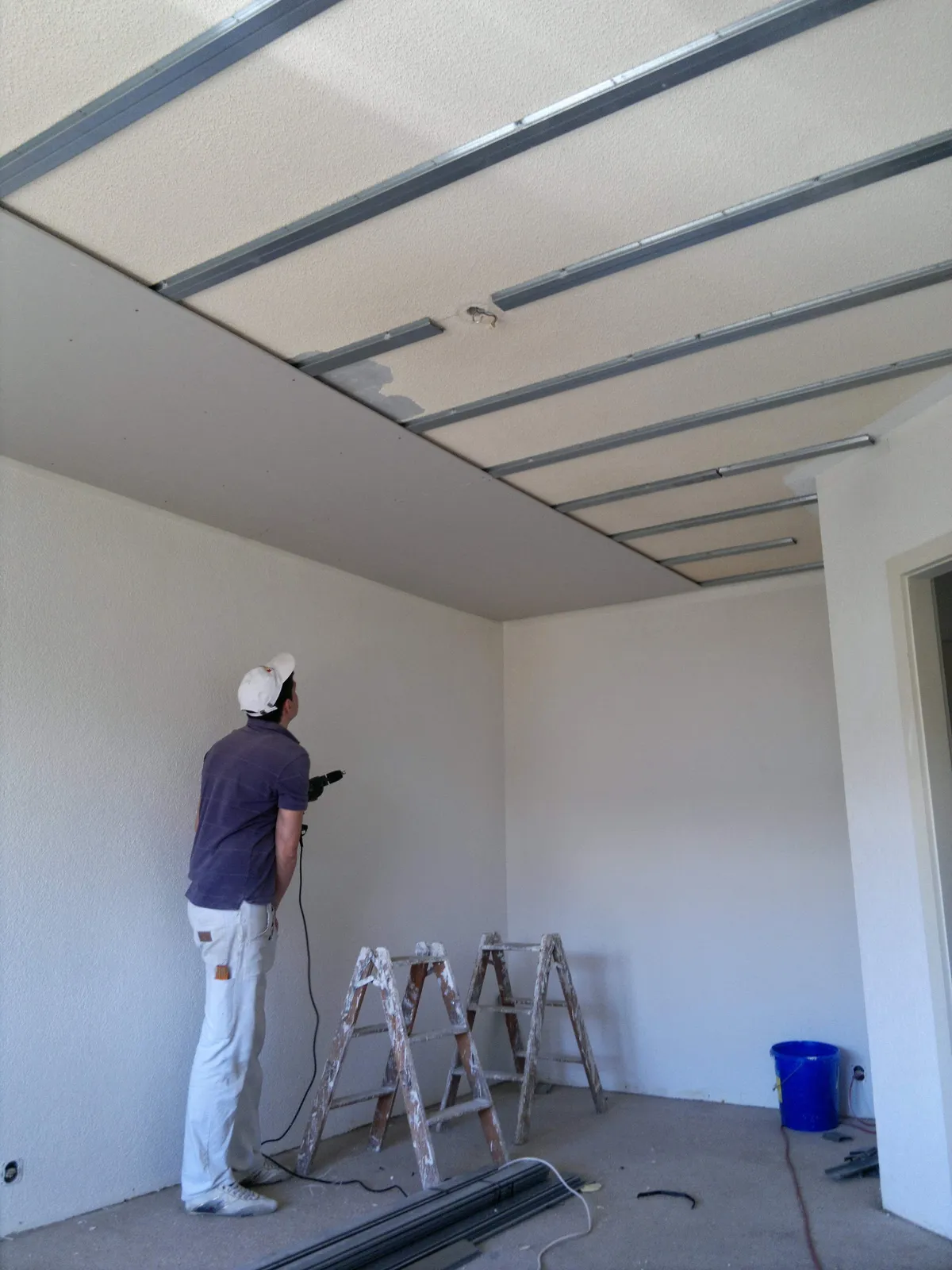 Installation de l'ossature métallique d'un faux plafond dans l'angle d'une pièce, une étape de plafond suspendu avant la pose des plaques.