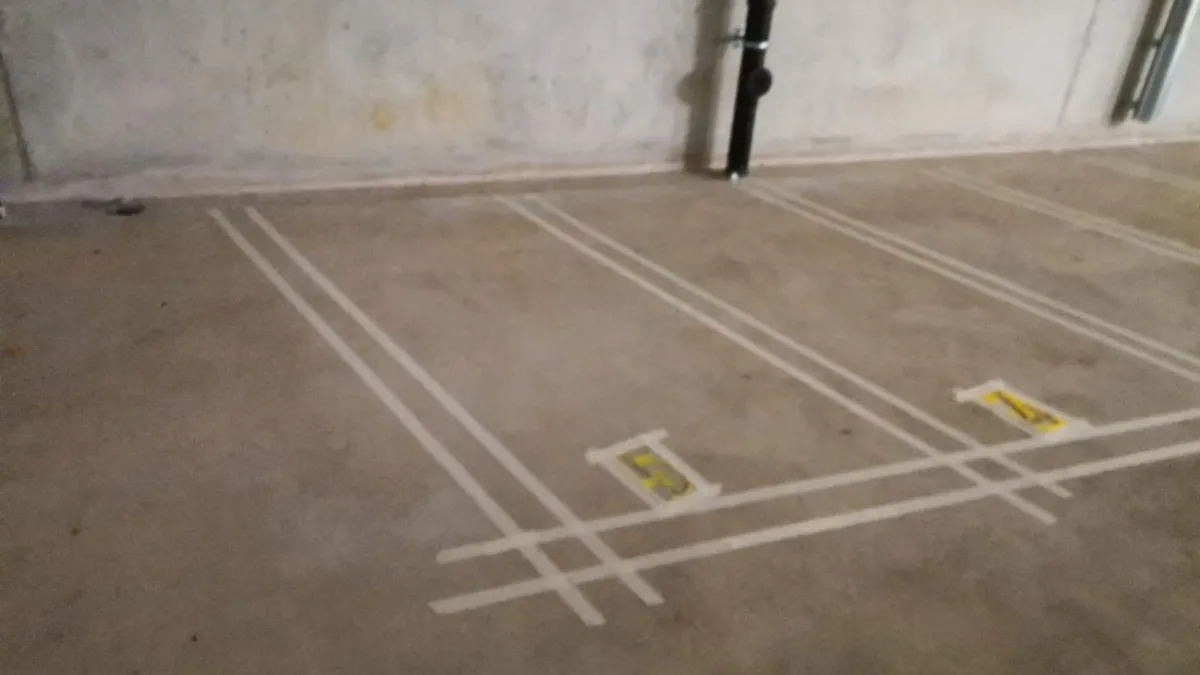 Places de parc intérieures délimitées par des doubles lignes blanches, marquage au sol sur dalle béton dans le canton de Vaud.