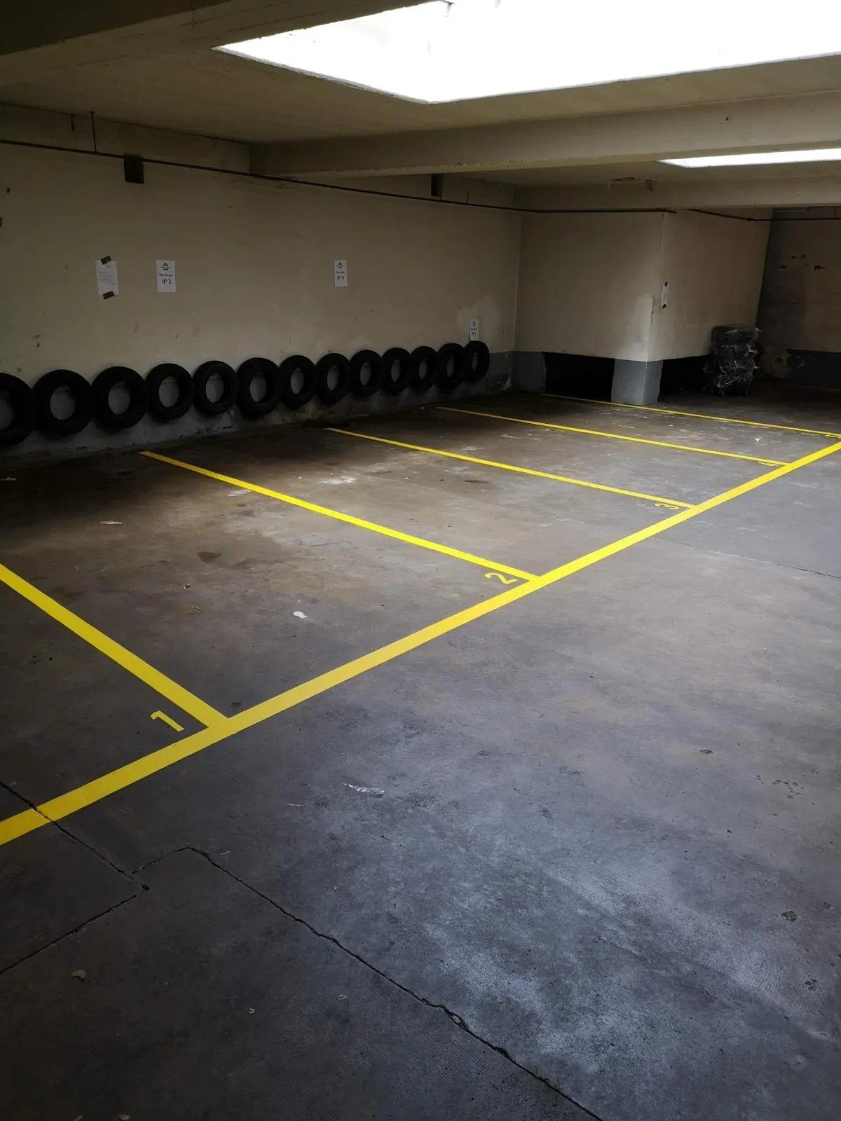 Places de parc numérotées au sol d'un garage collectif, lignes jaunes appliquées au pochoir sur béton par Peinture Casabene.