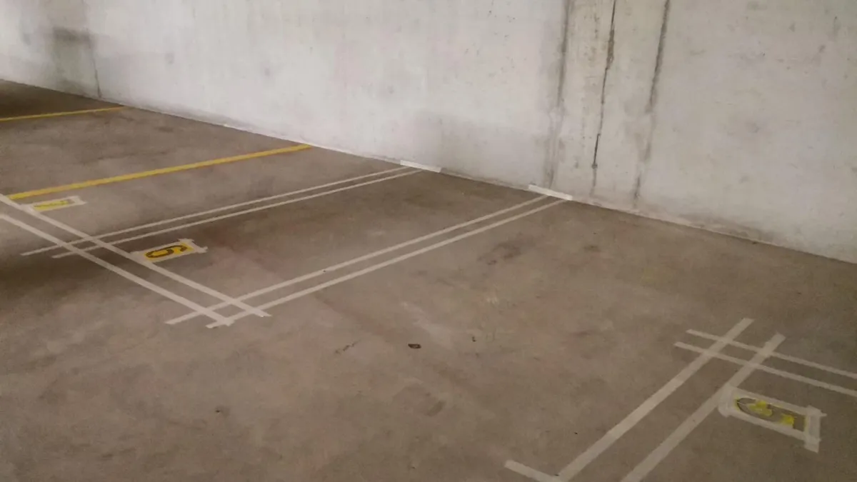 Marquage au sol d'un parking couvert, doubles lignes blanches et numéros jaunes appliqués sur une dalle béton dans le canton de Vaud.