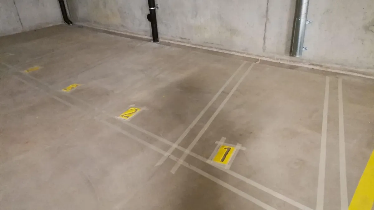 Numéros de places de parc au pochoir jaune sur béton lisse, marquage au sol réalisé en intérieur par une entreprise de peinture.