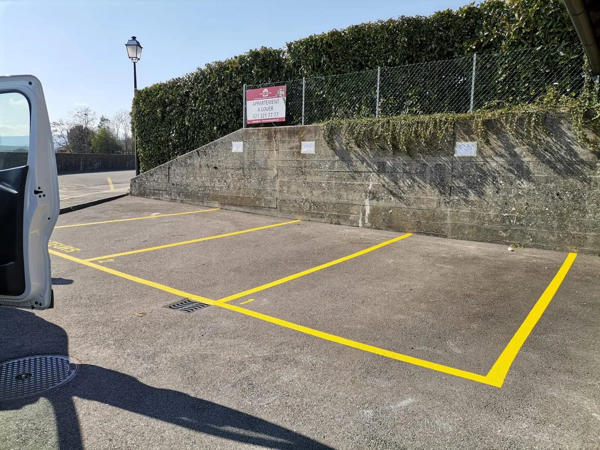 Places de parc extérieures délimitées par des lignes jaunes tracées au sol.
