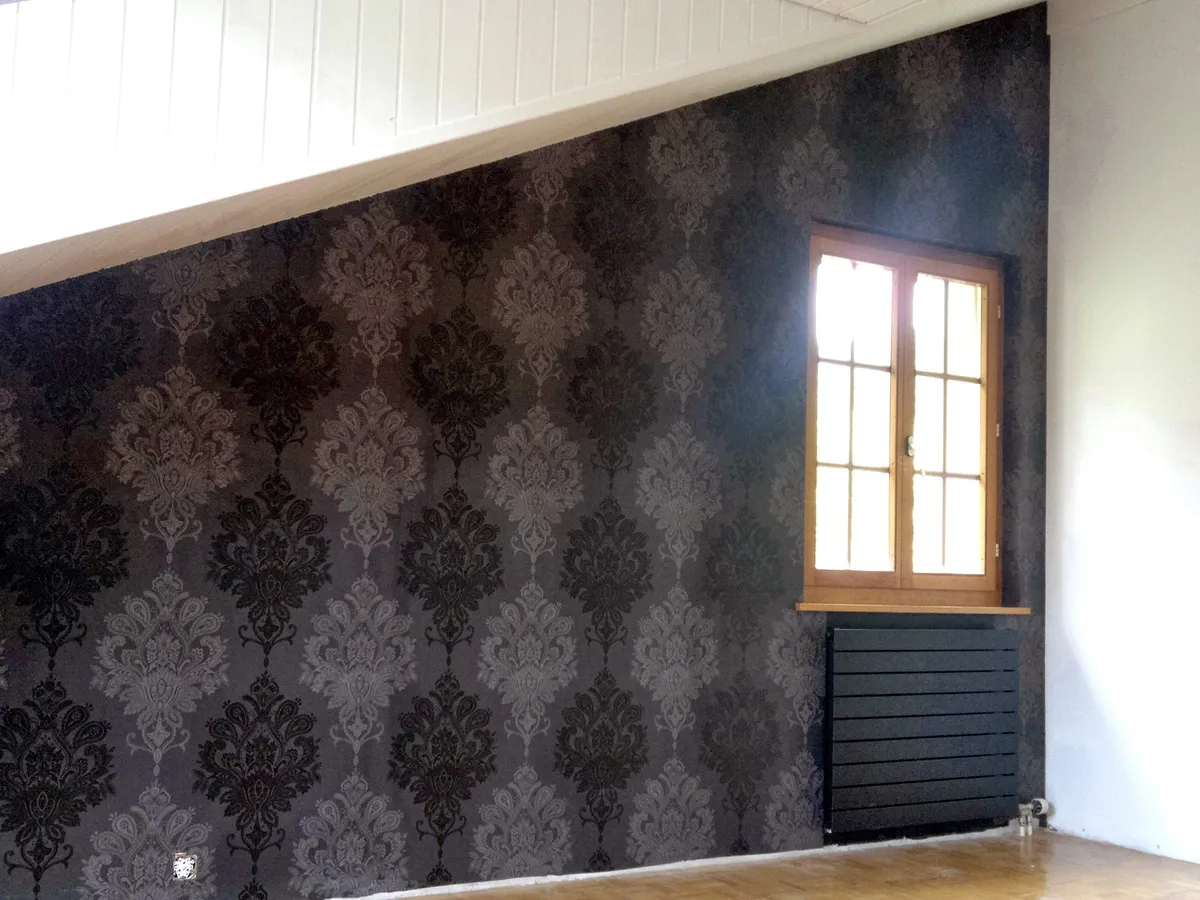 Papier peint damassé noir et argenté terminé près d'une fenêtre en bois et d'un parquet.