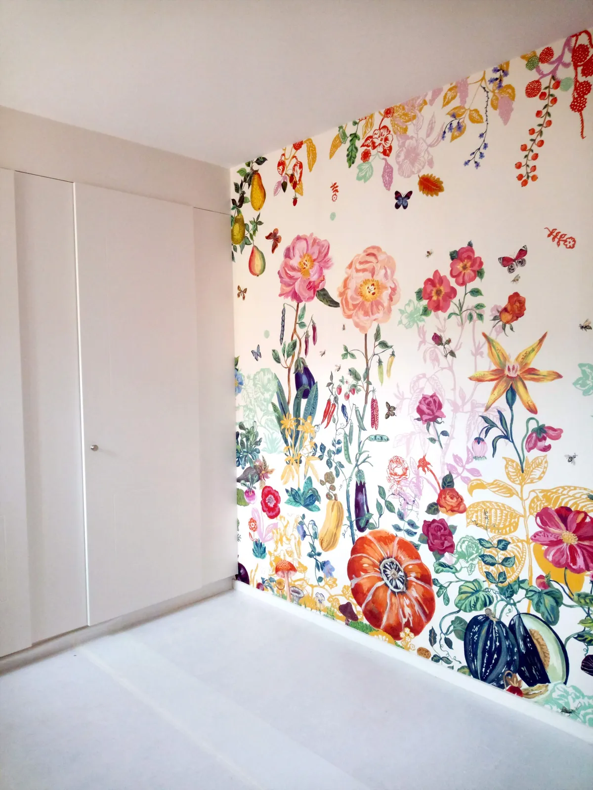 Angle de pièce avec porte blanche et papier peint fleuri remontant jusqu'au plafond, une pose réalisée par Peinture Casabene Sàrl.