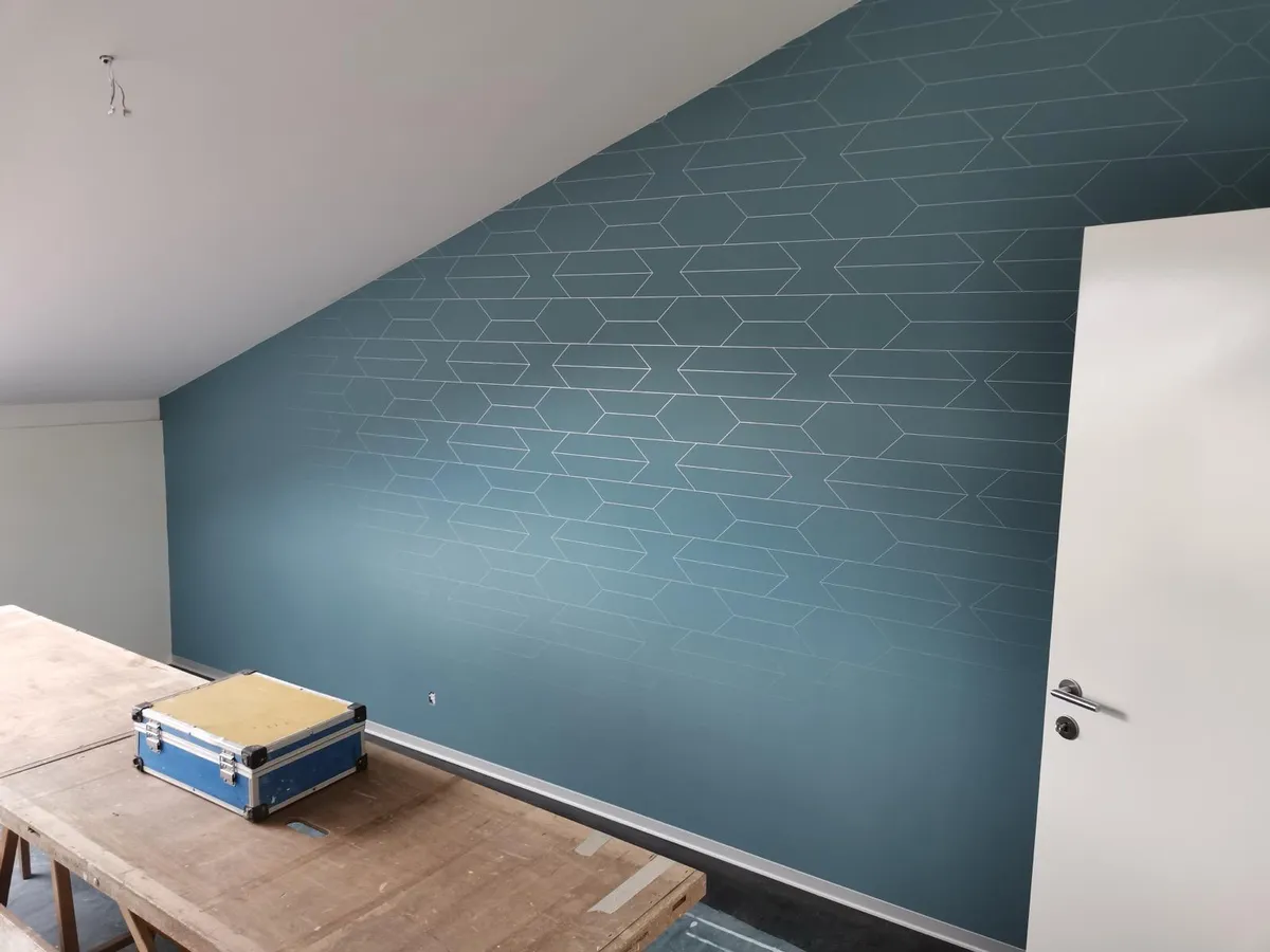 Mur sous rampant tapissé d'un papier peint géométrique bleu canard à liserés clairs, décoration intérieure dans une pièce de combles.