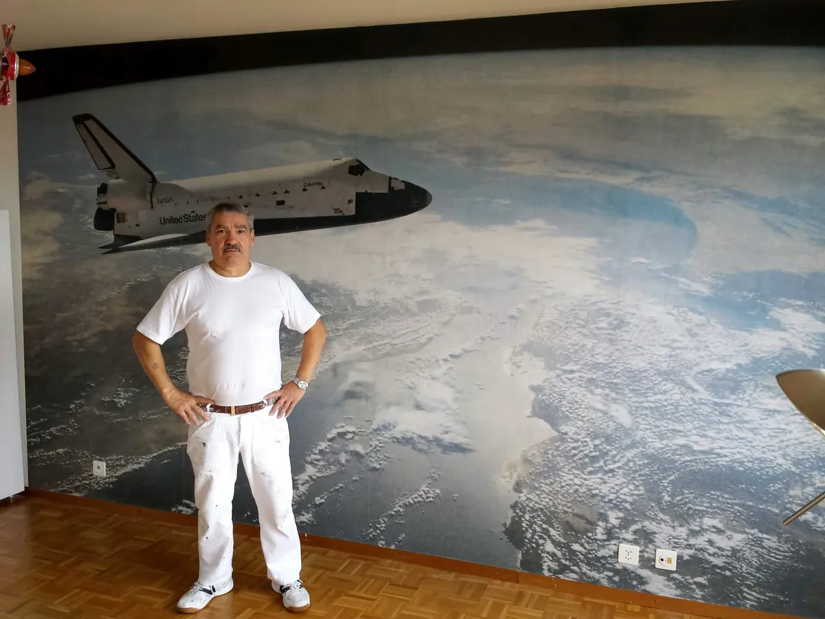 Peintre debout devant un papier peint panoramique de navette spatiale entièrement posé.