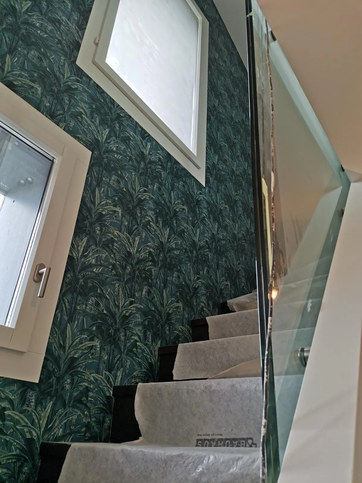 Escalier aux marches protégées bordé d'un papier peint tropical, chantier de décoration intérieure dans le canton de Vaud.