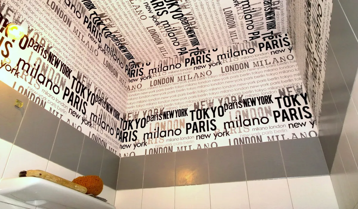 Papier peint à motif de villes posé dans une salle de bain, outils de tapissier encore présents, un chantier de l'atelier Peinture Casabene.