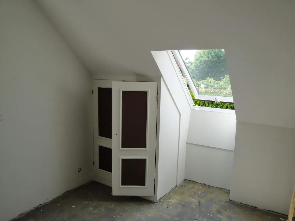 Armoire blanche à panneaux marron installée sous des combles, avec un velux ouvert.