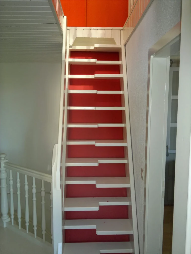 Escalier en bois aux marches rouges et rambarde blanche, un mur orange en arrière-plan, une peinture de boiseries signée Peinture Casabene.