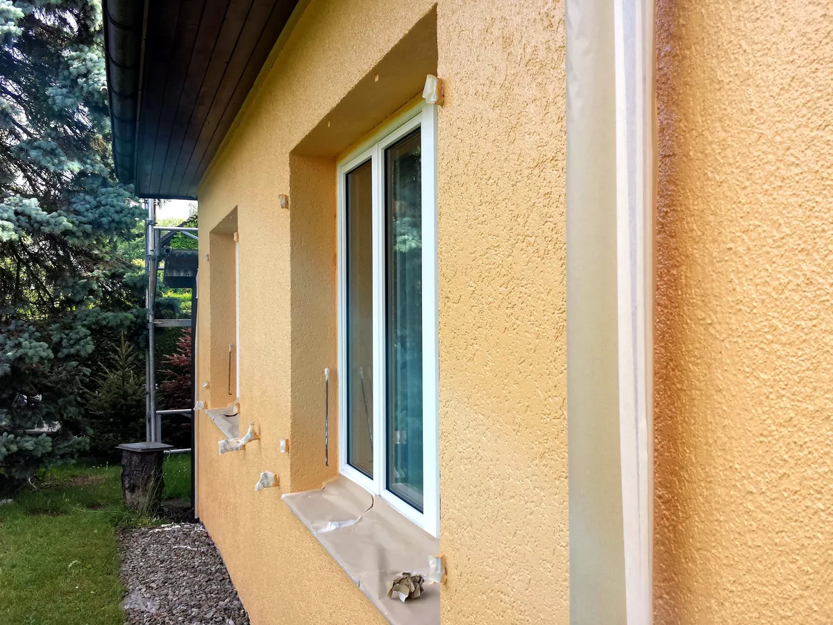 Façade beige terminée autour d'une fenêtre, avec le ruban de protection encore posé sur le rebord.