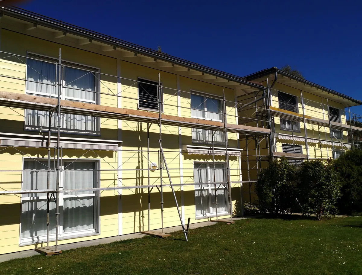 Immeuble jaune échafaudé vu depuis la pelouse, ciel bleu dégagé, un ravalement de façade en cours de réalisation.