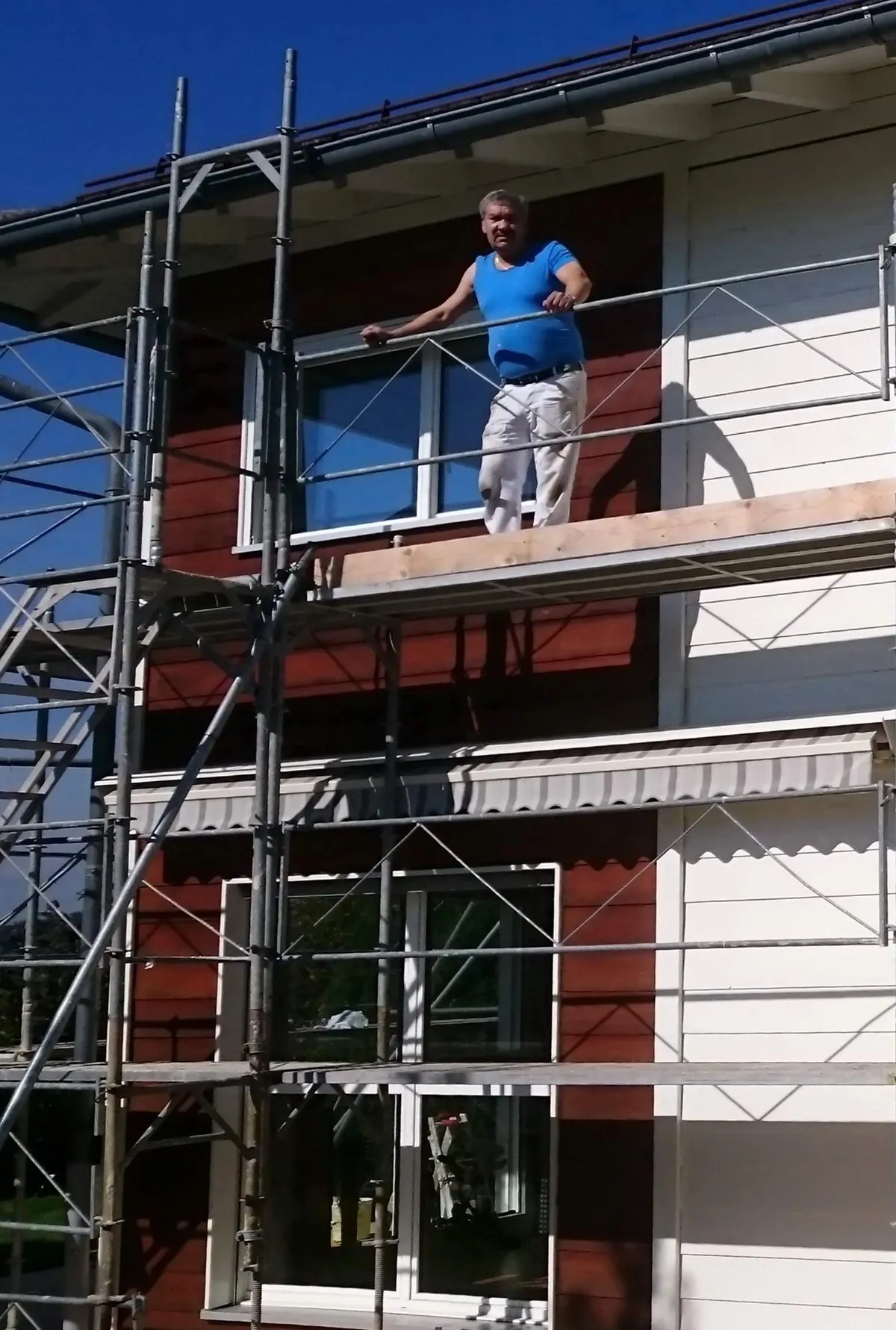 Peintre en pause sur un échafaudage, façade rouge et blanche en arrière-plan, pendant un chantier de rénovation de façade signé Peinture Casabene.