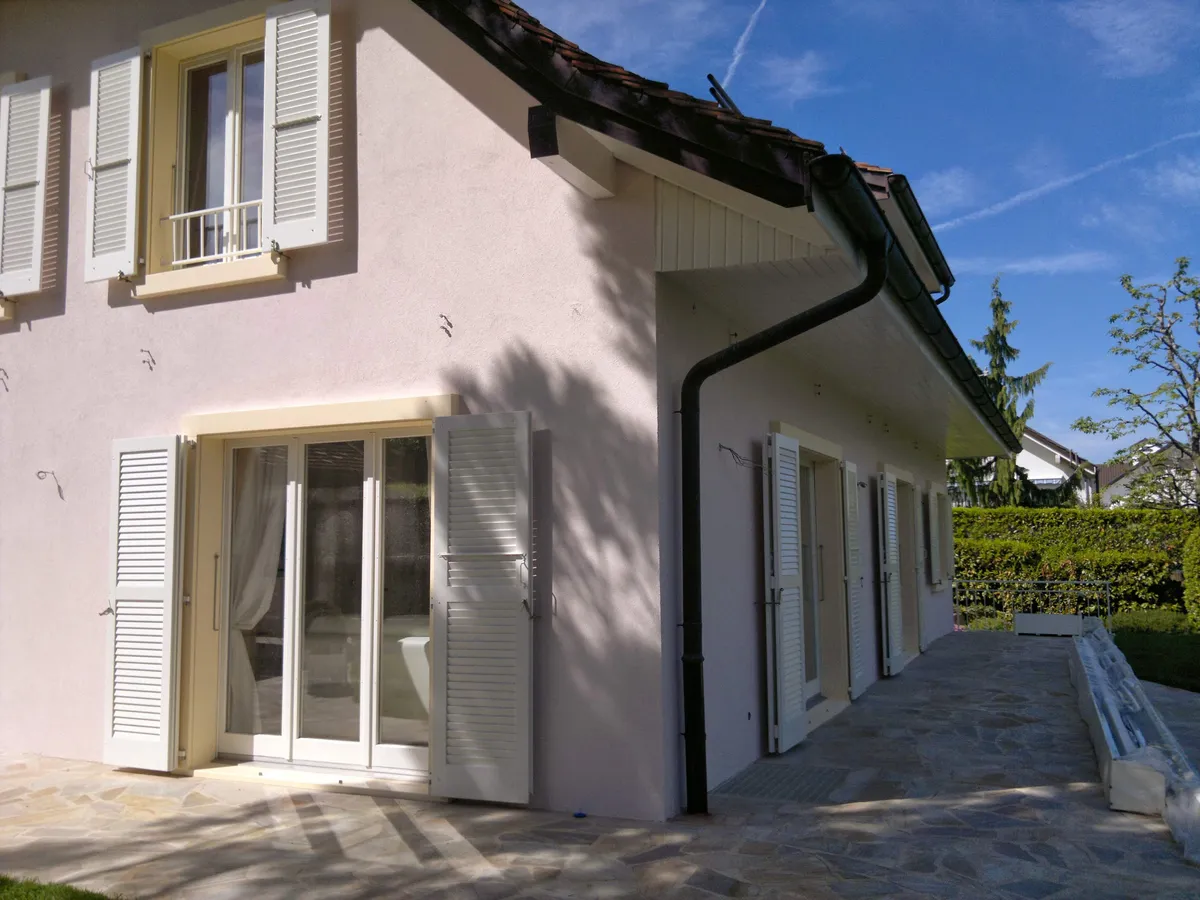 Façade rose pâle terminée autour d'une baie vitrée ouvrant sur une terrasse.