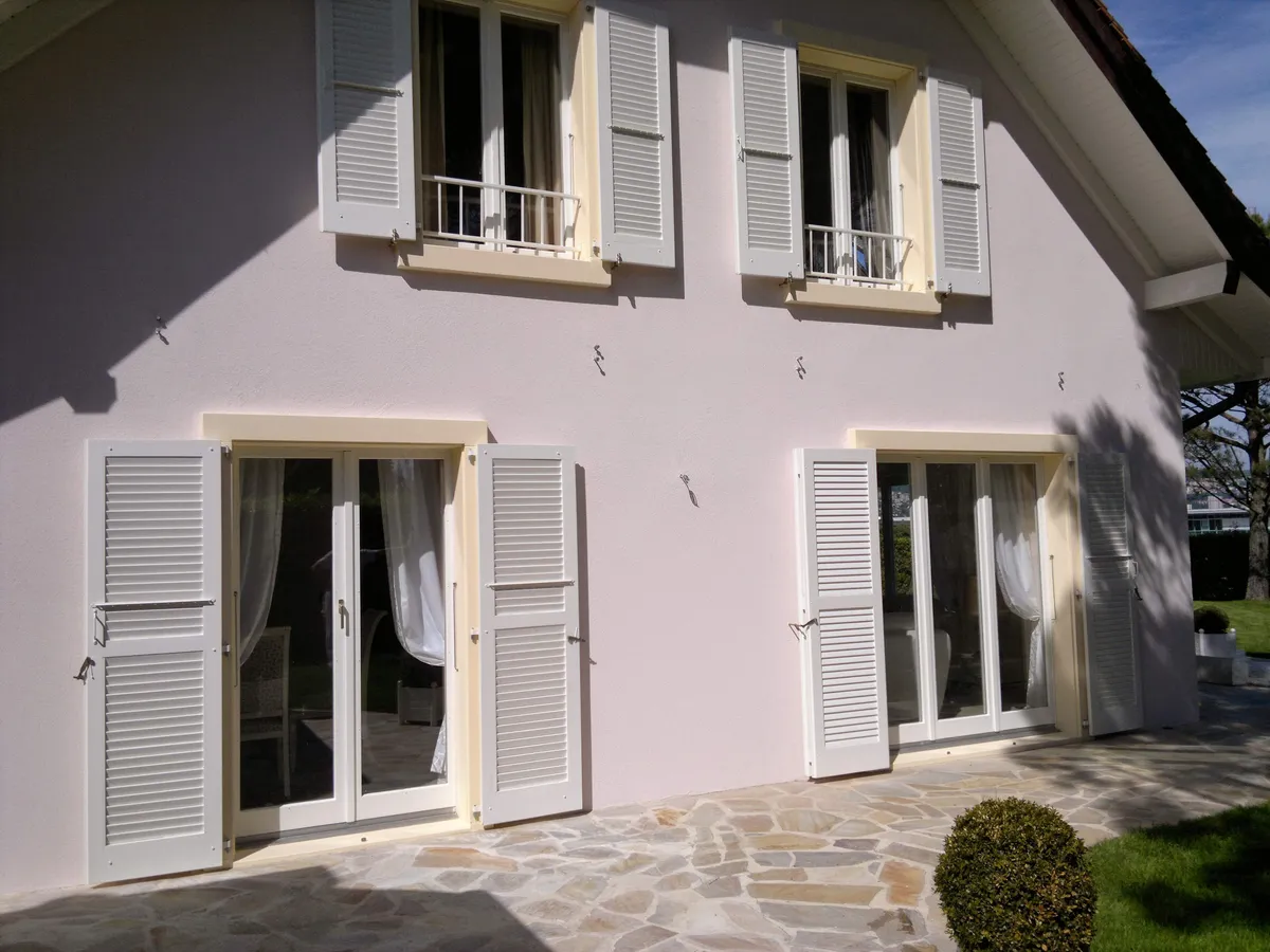 Façade terminée aux persiennes fermées, bordée d'une terrasse en pierre de plain-pied.