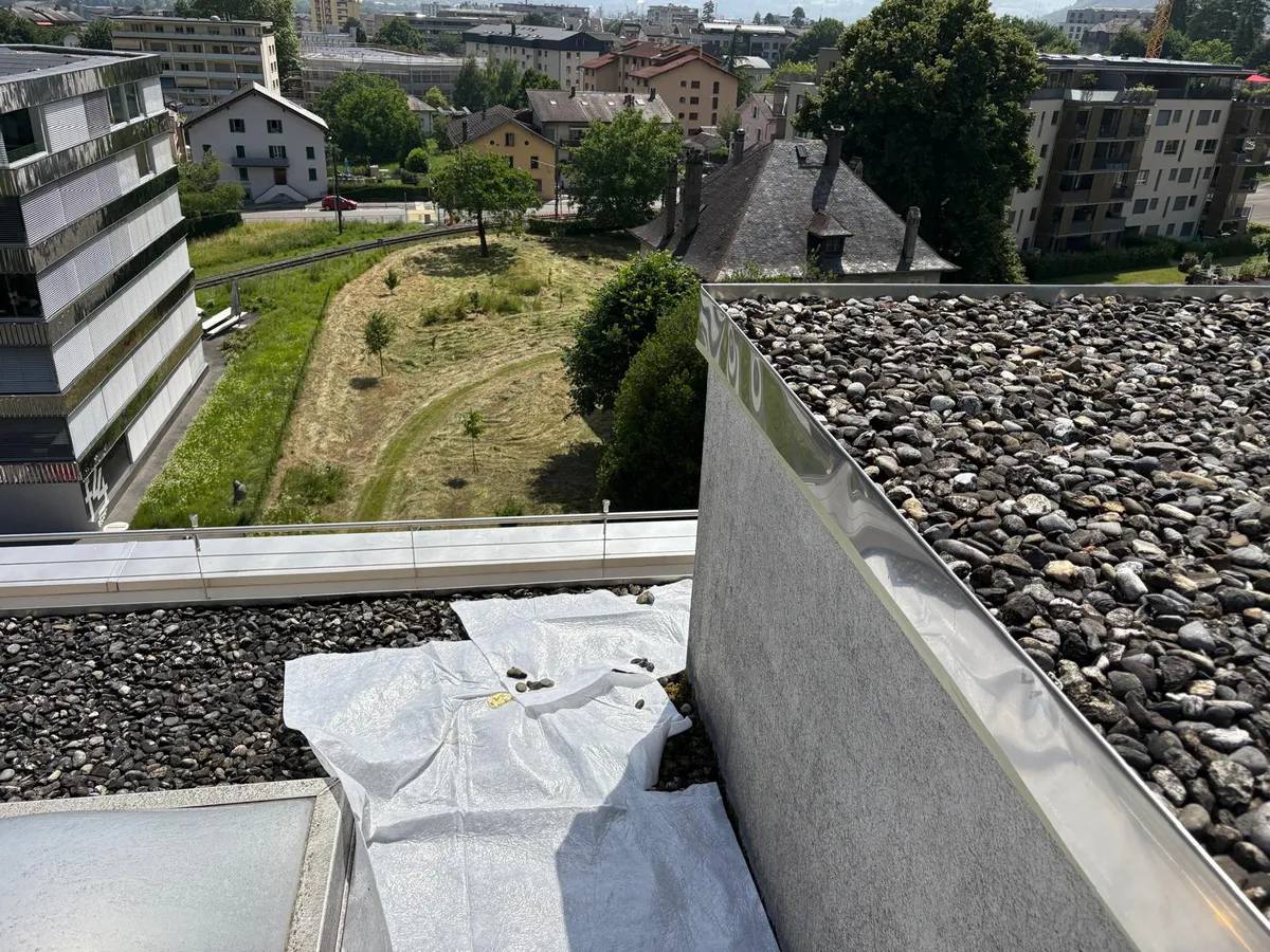 Toiture plate en gravier protégée par une bâche pendant des travaux de peinture de façade, couvertine métallique en périphérie.