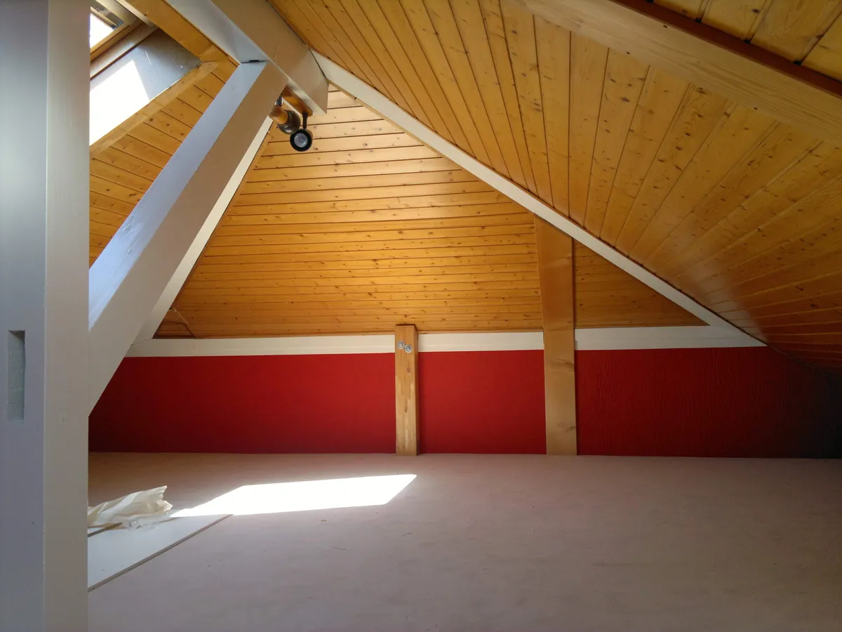 Comble vide aux murs rouges, avec une charpente en bois apparente et une lucarne au plafond.