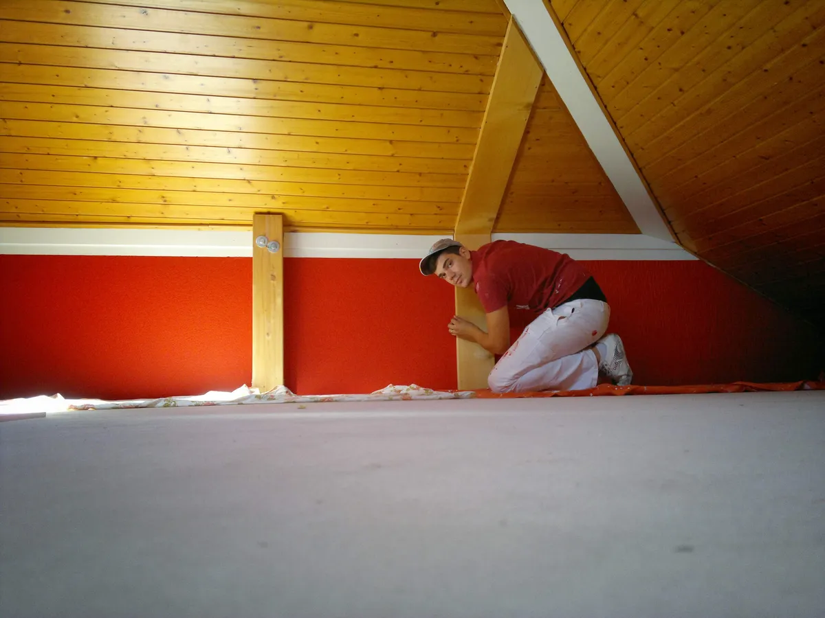 Peintre reprenant le bas d'un mur en combles, une retouche localisée plutôt qu'une remise en peinture complète.
