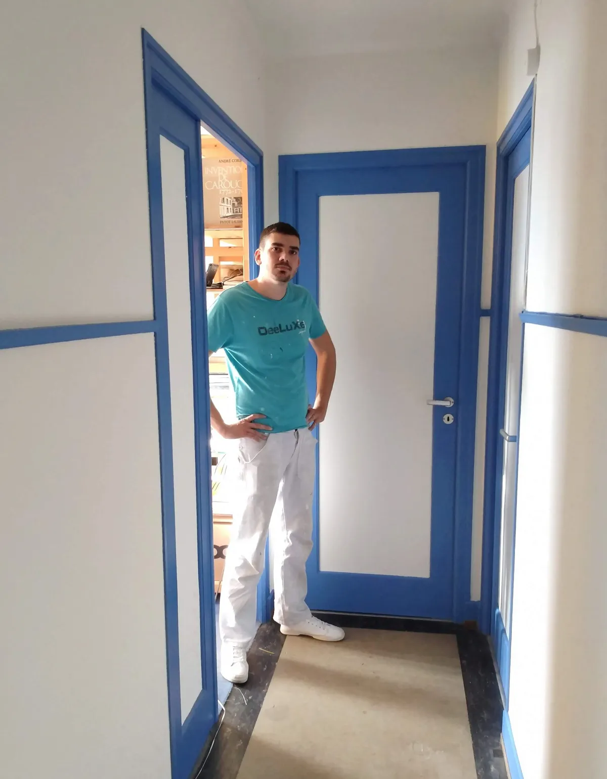 Un employé pose devant une porte à chambranle bleu fraîchement repeinte dans un couloir, mise en peinture achevée par Peinture Casabene.