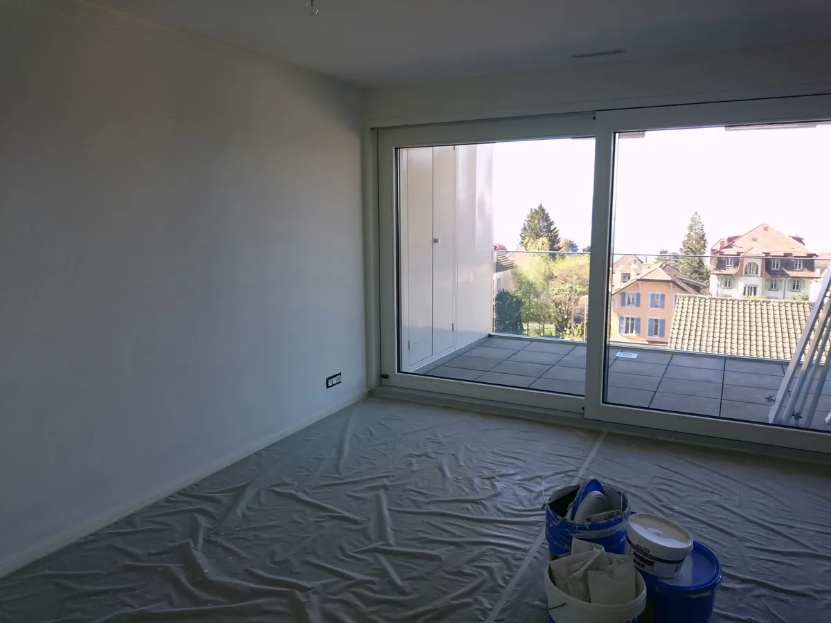 Pièce vide aux murs repeints en beige clair, avec une grande baie vitrée donnant sur l'extérieur.
