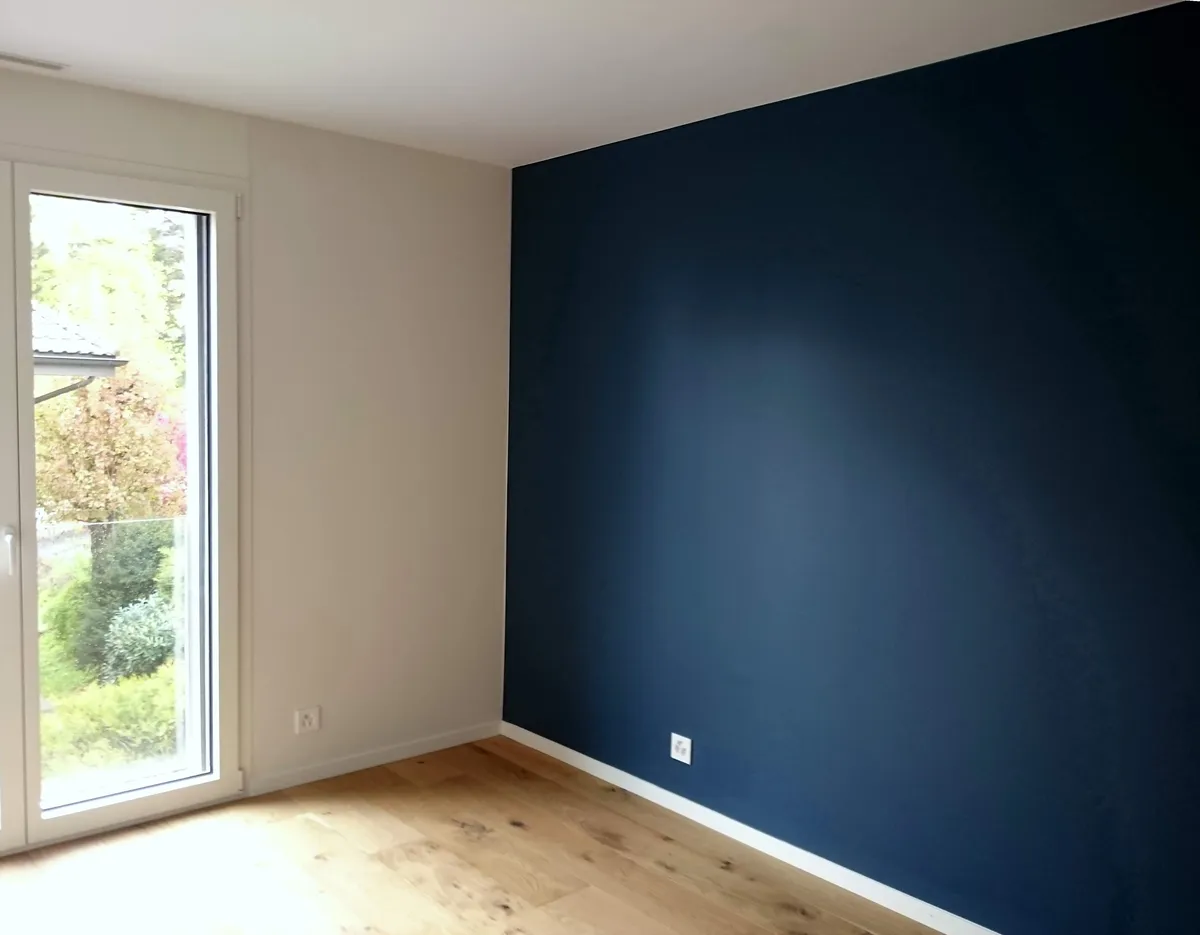 Mur bleu marine et parquet dans une pièce ouverte sur le jardin.