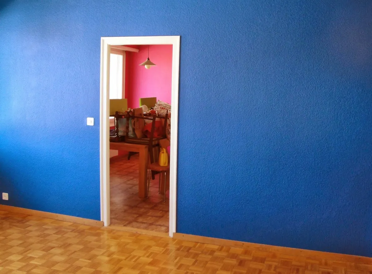 Salle à manger dont le mur est peint en bleu, au-dessus d'un parquet clair.