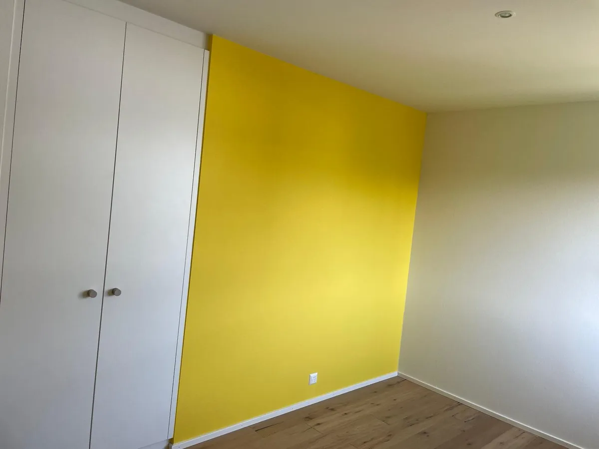 Chambre au mur jaune avec une armoire blanche, remise en peinture dans un logement meublé.