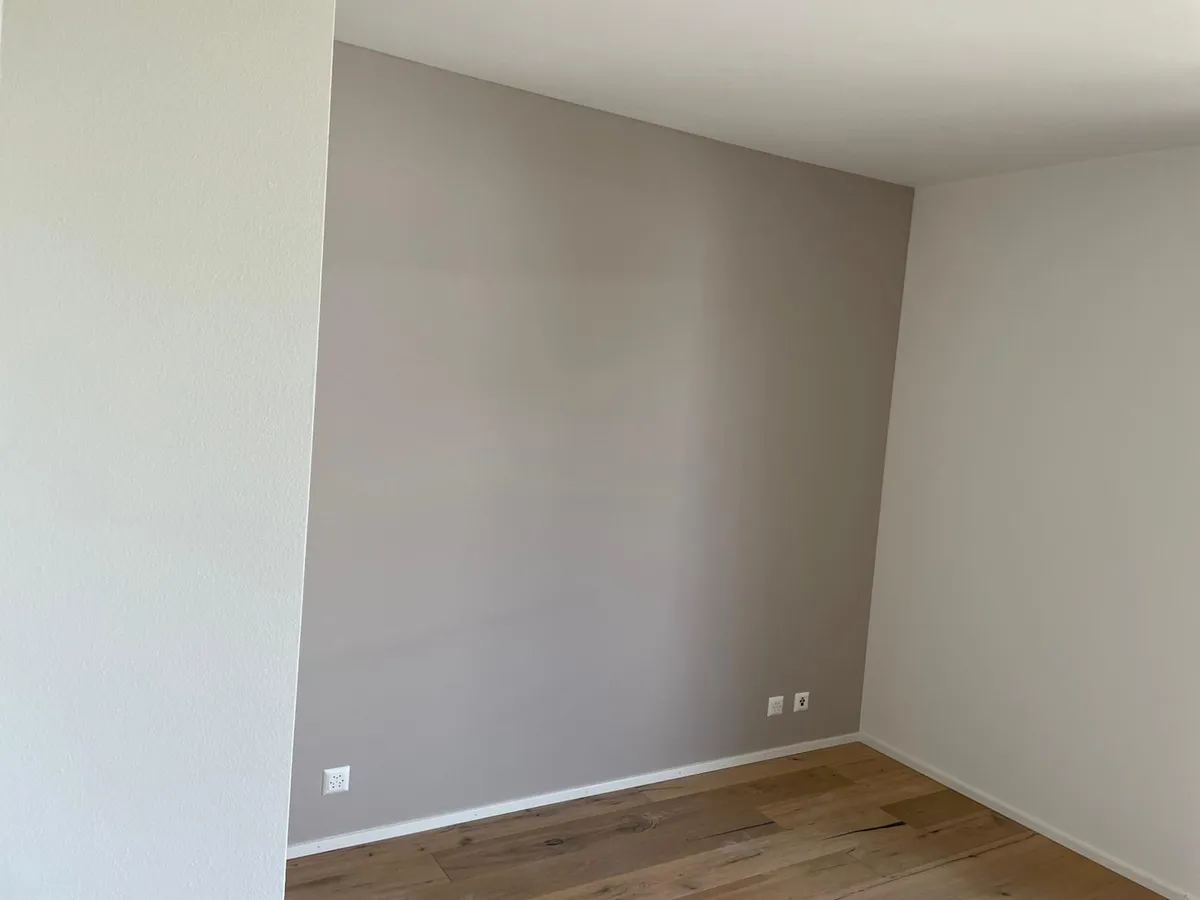 Chambre aux murs taupe fraîchement repeints et parquet clair, logement prêt à être rendu.