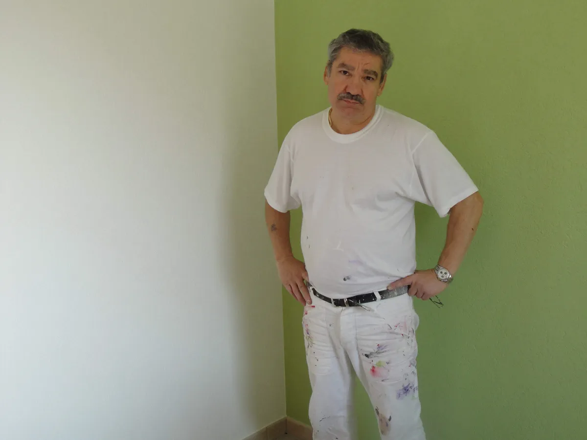 Pièce vide aux murs vert anis, peintre au travail avant le retour à une teinte neutre.