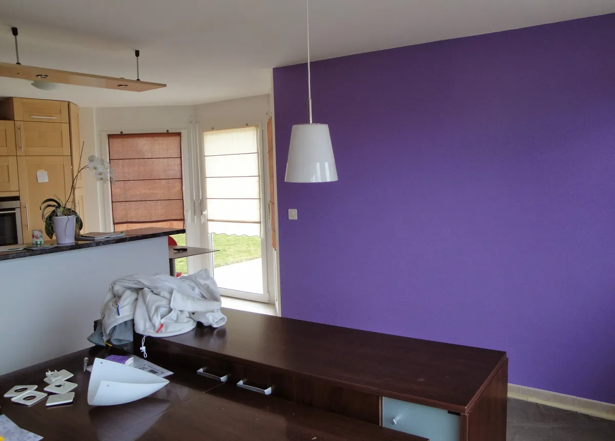 Cuisine ouverte sur le séjour avec un mur violet et une suspension blanche, après mise en peinture.