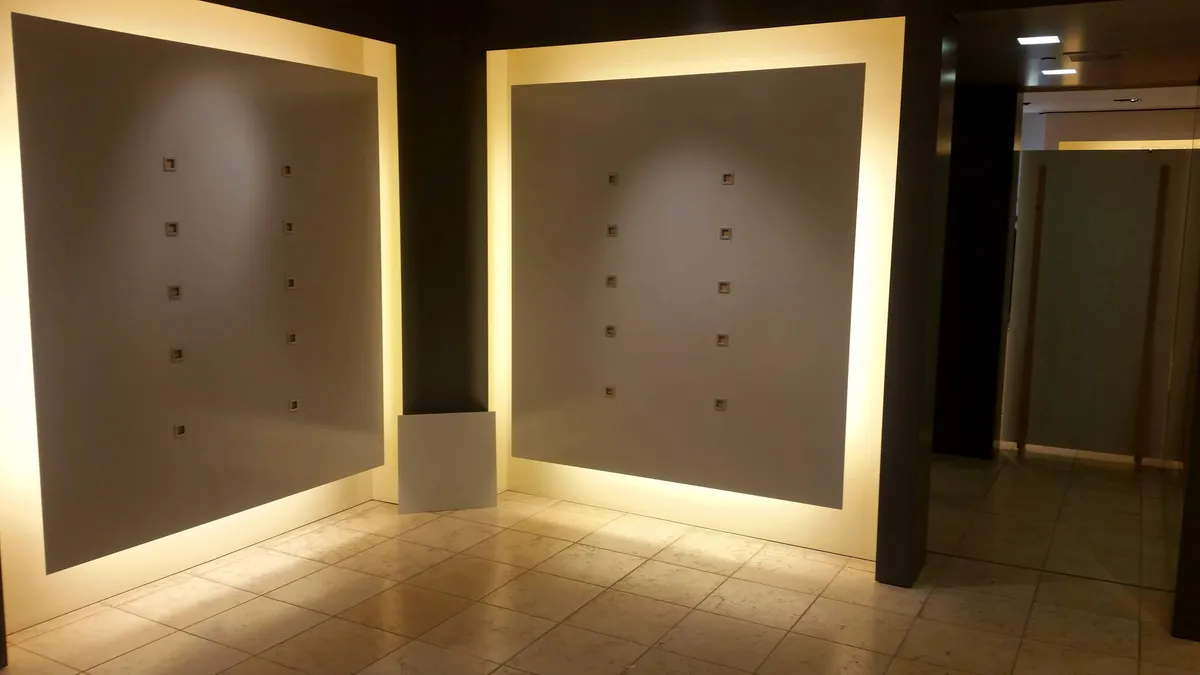 Niches grises éclairées aménagées dans un mur, au-dessus d'un sol en marbre.