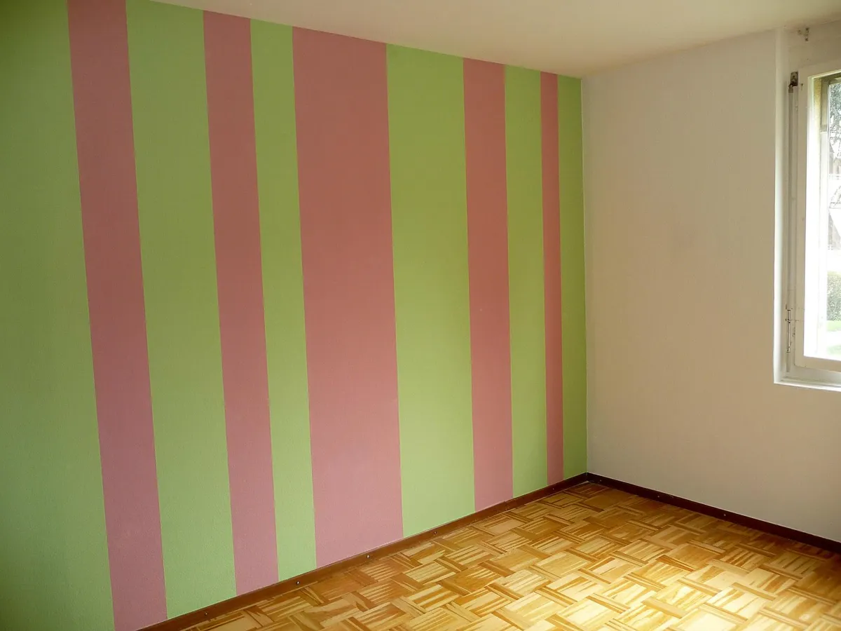 Chambre terminée aux murs rayés verticalement de vert et de rose, avec un parquet au sol, exemple de mise en peinture soignée.