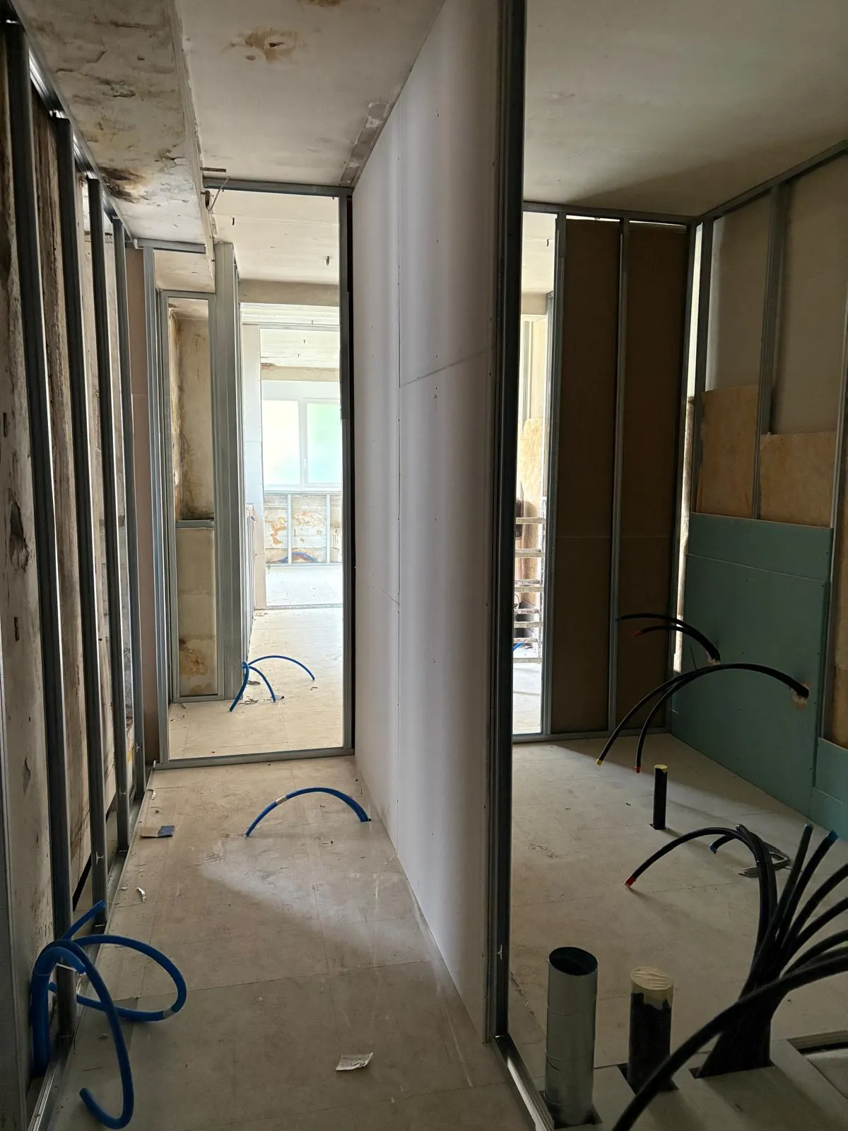 Couloir dont une cloison est déjà fermée en plaques de plâtre, gaines électriques en attente au sol, chantier de plâtrerie dans le canton de Vaud.