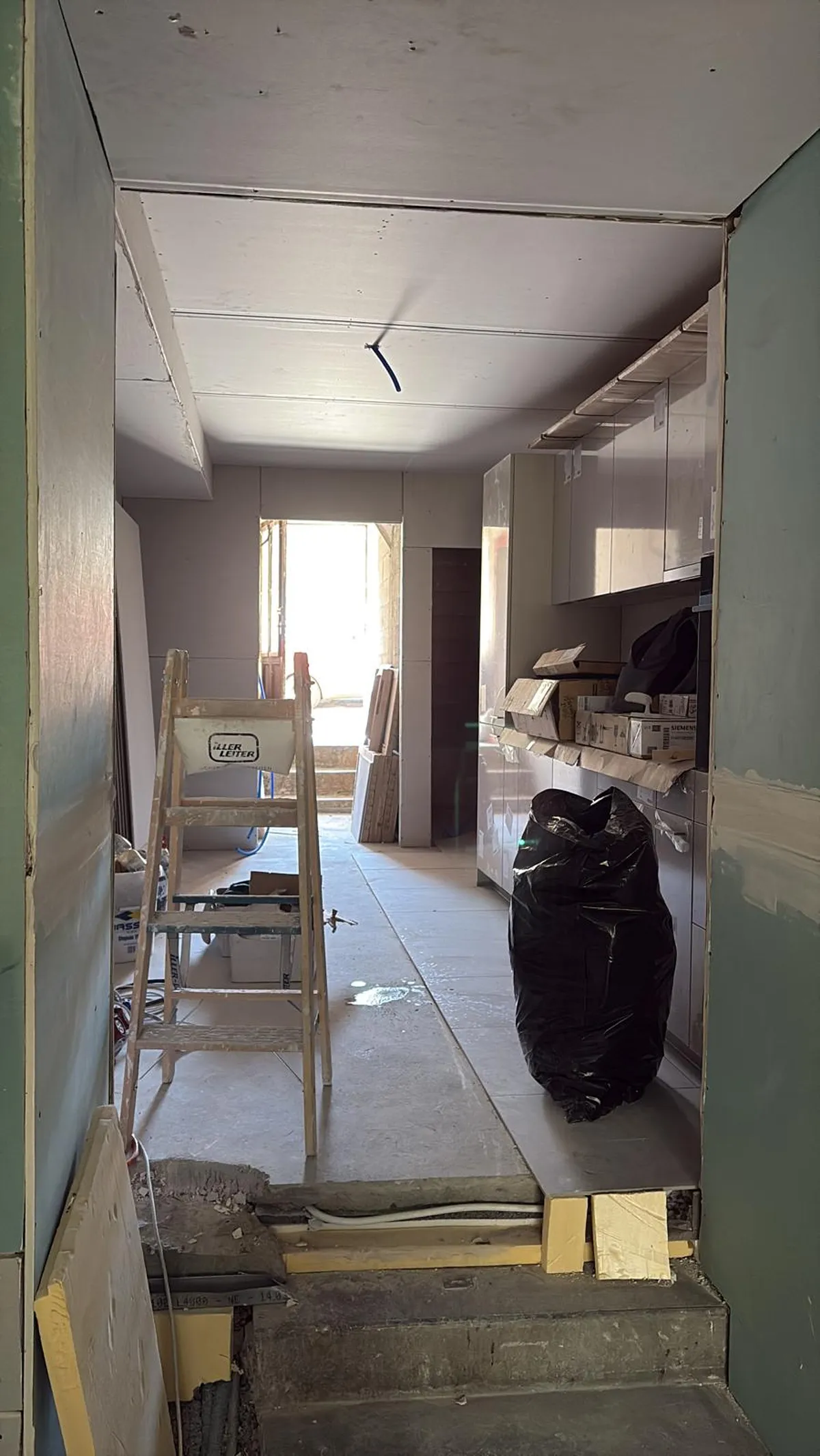 Couloir et cuisine en rénovation avec plafond plaqué et seuils protégés, chantier de plâtrerie et de peinture en région lausannoise.