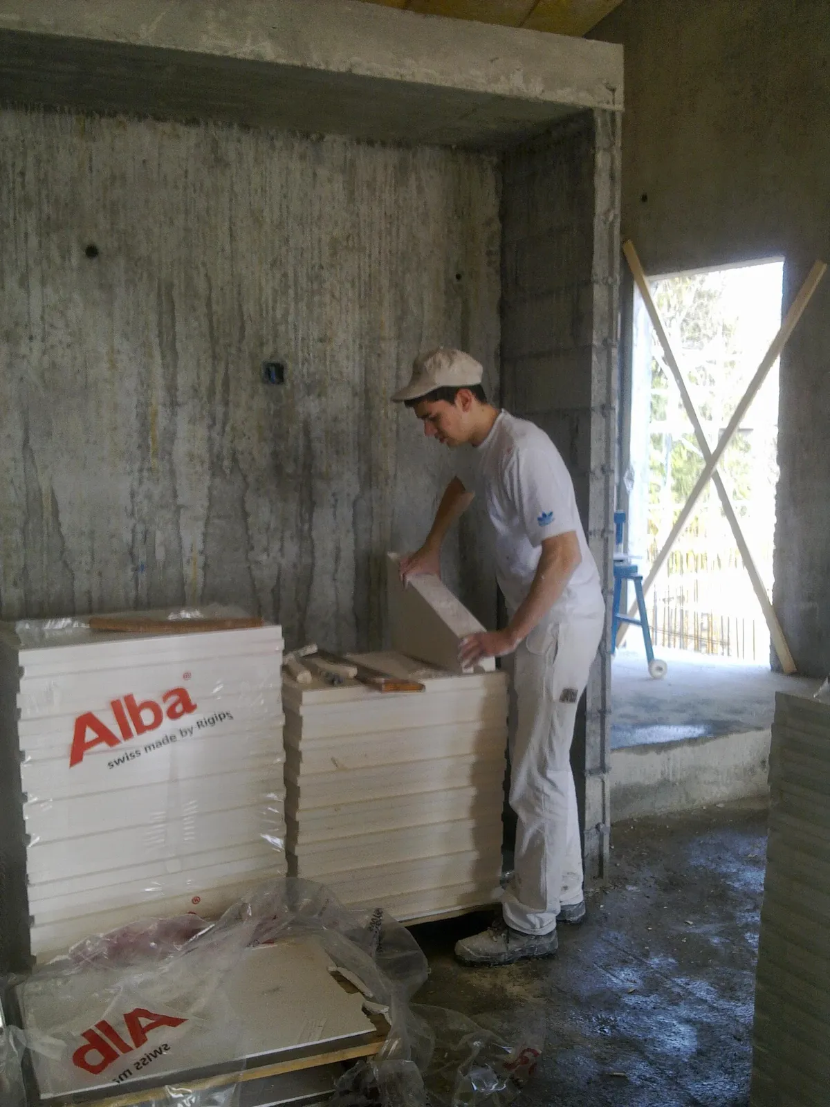 Un poseur découpe une plaque de plâtre au sol dans une pièce en gros œuvre brut, pose de placoplâtre réalisée par l'équipe de Peinture Casabene.