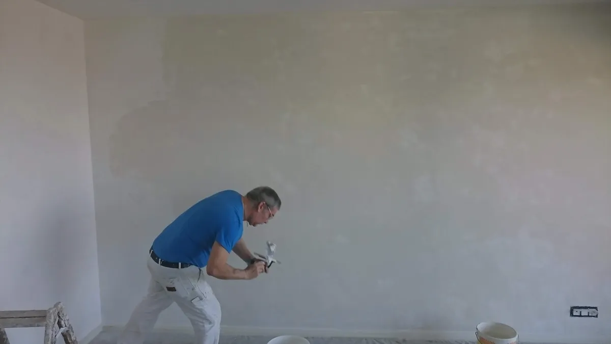Artisan en bleu de travail lissant l'enduit sur un mur clair dans un salon vide, une étape de plâtrerie réalisée par Peinture Casabene.