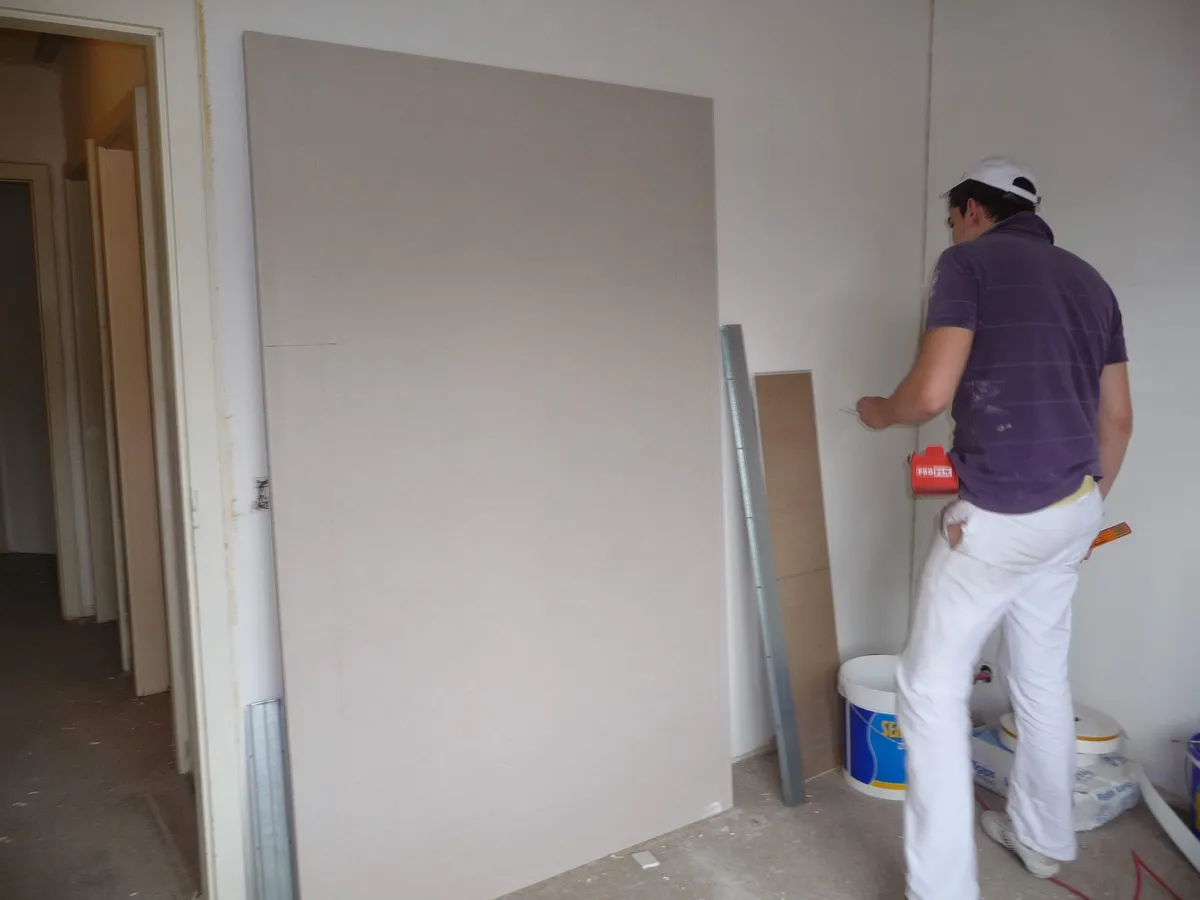 Ouvrier positionnant une grande plaque de plâtre contre une cloison en construction, une pose de placoplâtre assurée par Peinture Casabene.