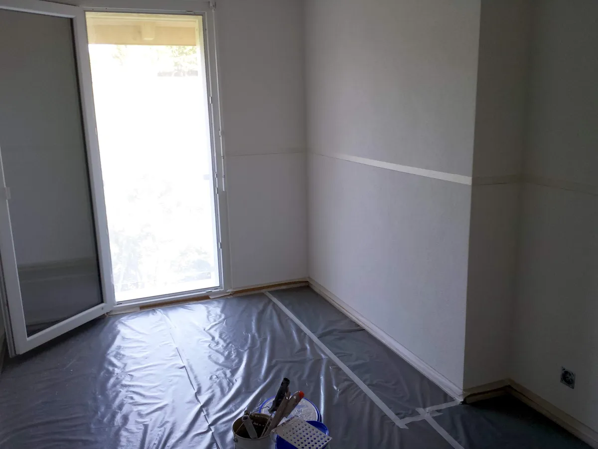 Sol protégé par une bâche et un ruban de masquage avant la peinture de la chambre, une préparation de chantier soignée.