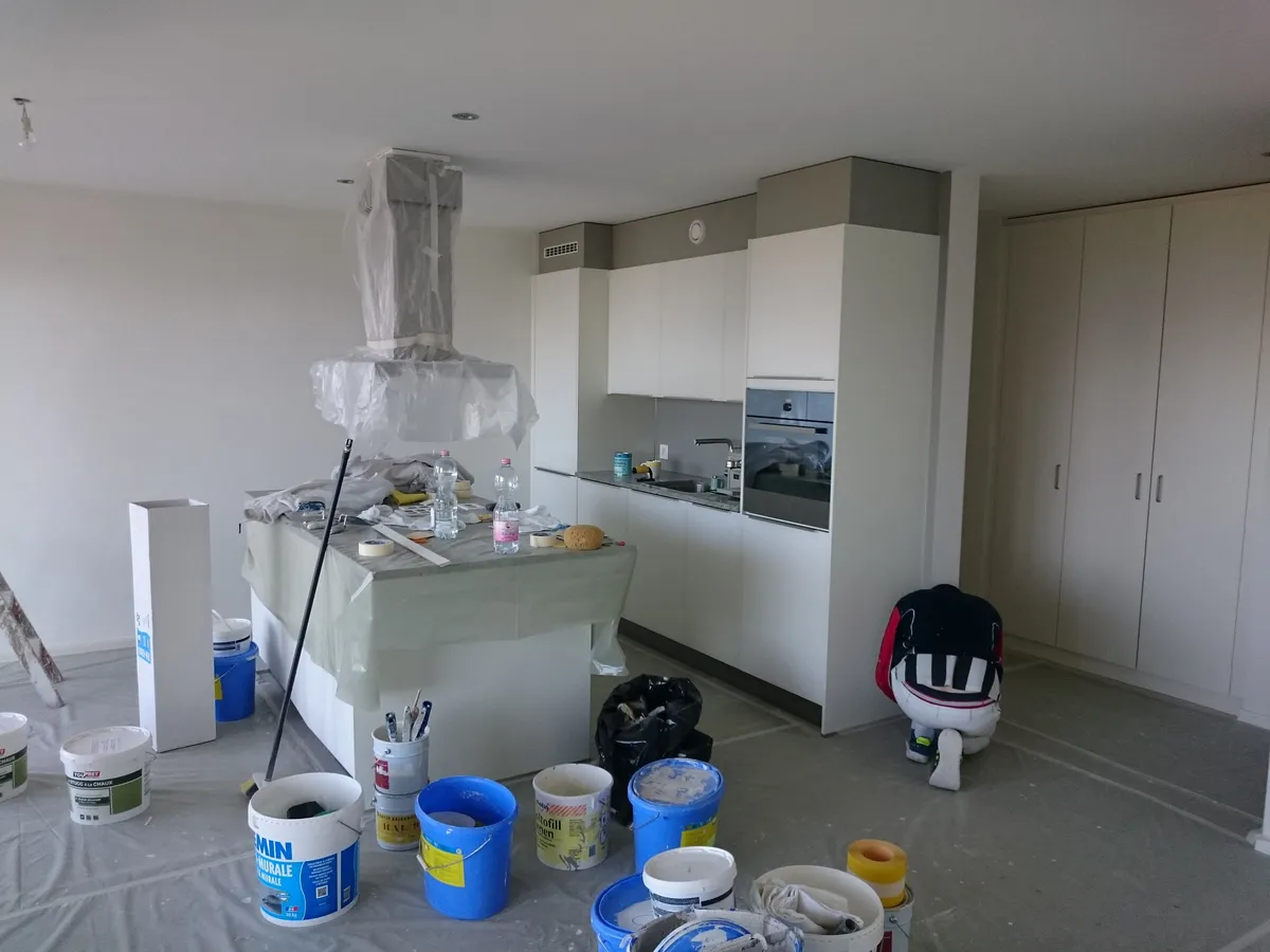 Cuisine en travaux, hotte protégée par un film plastique et matériel de peinture posé au sol.